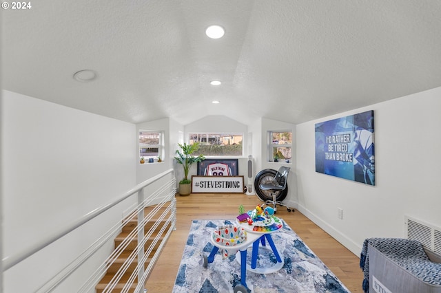 recreation room with lofted ceiling, a textured ceiling, and light hardwood / wood-style flooring