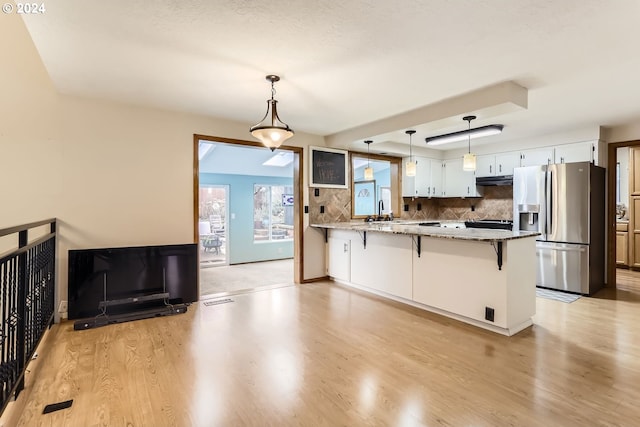 kitchen featuring white cabinetry, tasteful backsplash, stainless steel refrigerator with ice dispenser, kitchen peninsula, and a breakfast bar