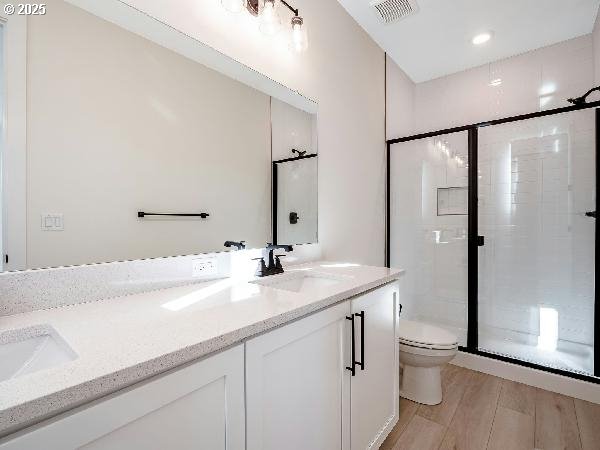 full bathroom featuring toilet, a sink, visible vents, a shower stall, and double vanity