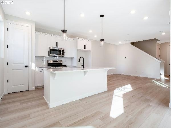 kitchen featuring white cabinets, appliances with stainless steel finishes, hanging light fixtures, a kitchen island with sink, and light countertops