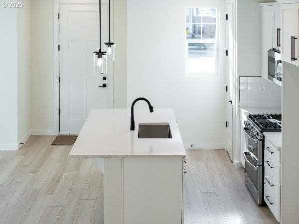 kitchen with appliances with stainless steel finishes, a kitchen island with sink, light countertops, white cabinetry, and a sink