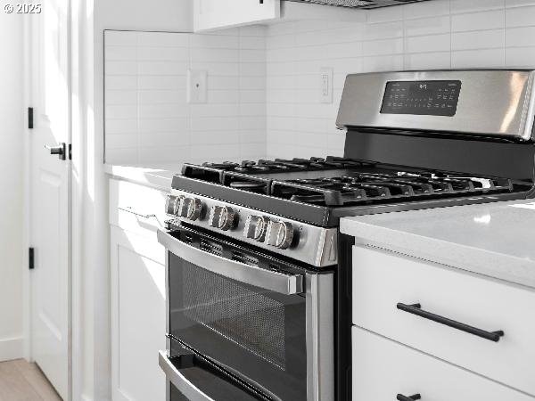 kitchen featuring range with two ovens, white cabinetry, backsplash, and light stone counters