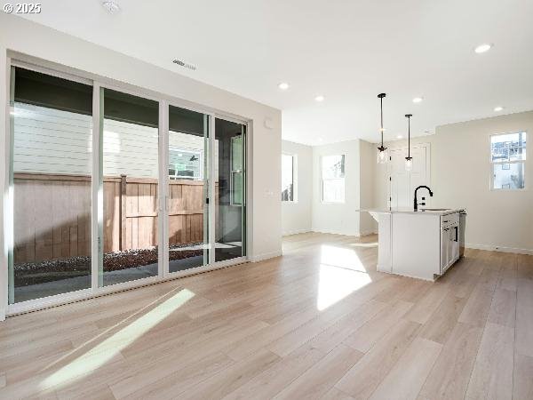 interior space with a center island with sink, white cabinets, decorative light fixtures, a sink, and a wealth of natural light