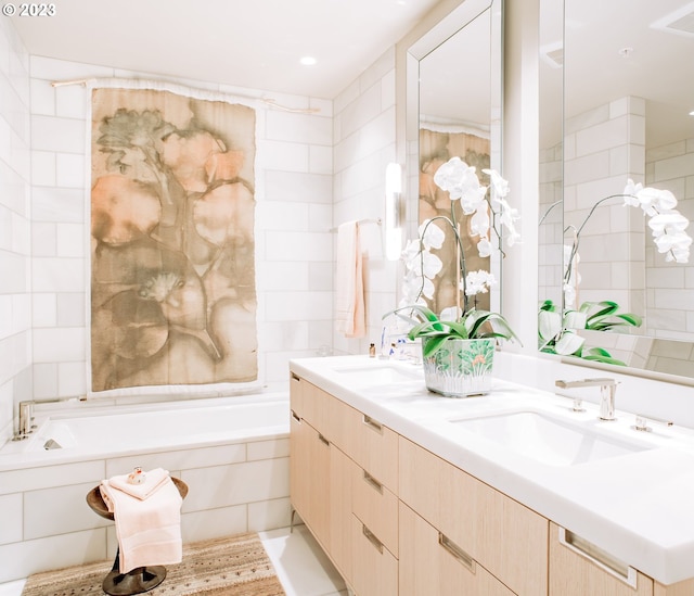 full bath with double vanity, tiled tub, tile walls, and a sink