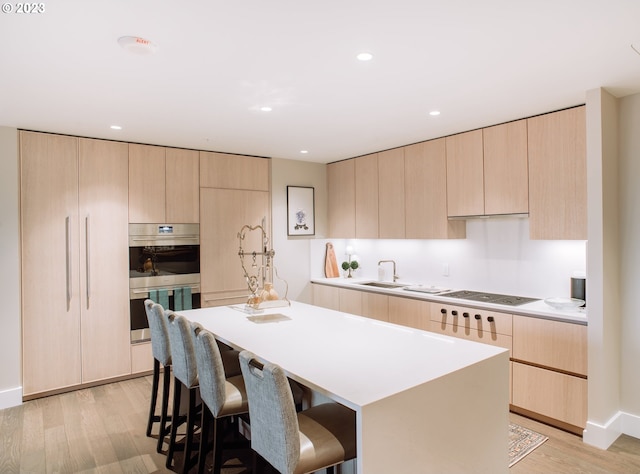 kitchen featuring double oven, light brown cabinets, electric cooktop, and a center island