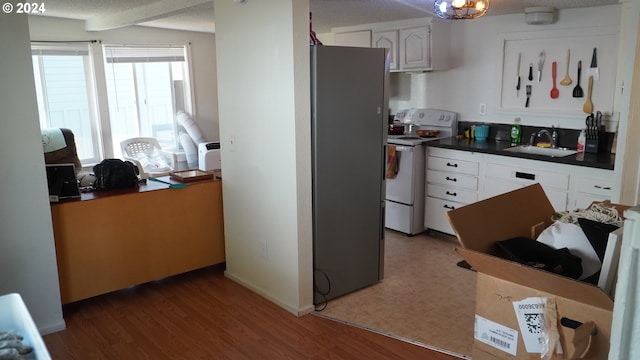 kitchen with white cabinetry, wood-type flooring, sink, stainless steel fridge, and white range with electric cooktop