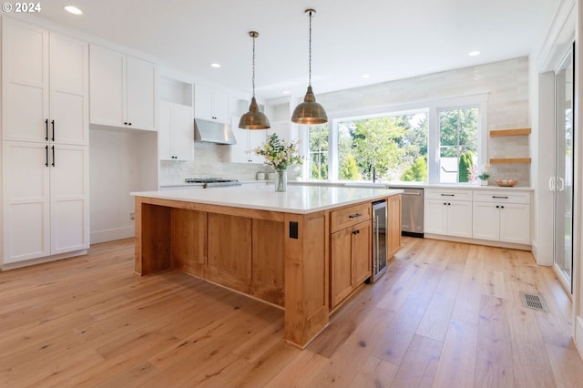 kitchen with white cabinets, light wood-type flooring, a large island with sink, and tasteful backsplash