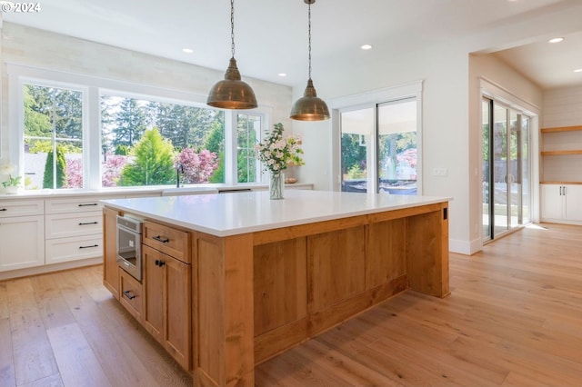 kitchen with a kitchen island, white cabinets, decorative light fixtures, and light wood-type flooring