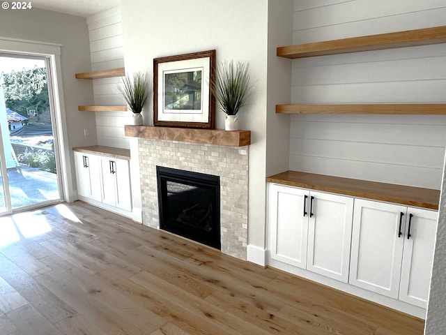 unfurnished living room featuring a fireplace, light wood-type flooring, and wooden walls