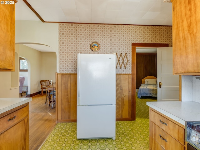 kitchen with white fridge, crown molding, wooden walls, light wood-type flooring, and range