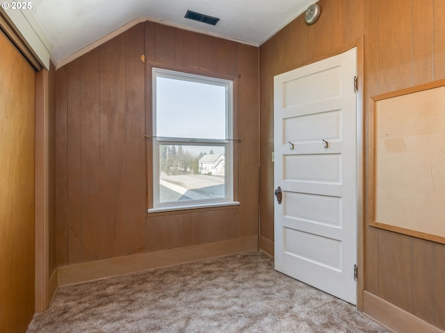 interior space featuring light colored carpet, wood walls, and vaulted ceiling