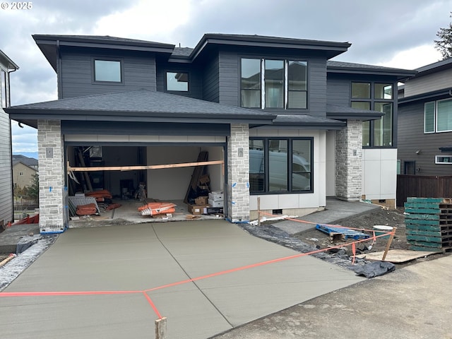 rear view of property with a shingled roof and concrete driveway