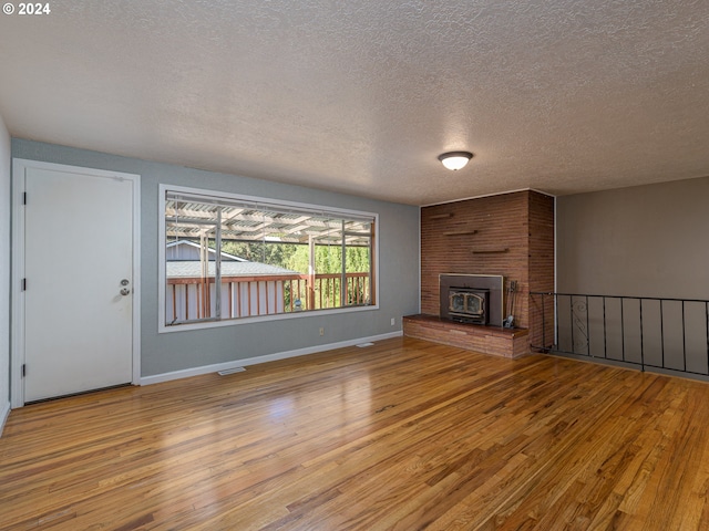 unfurnished living room with a brick fireplace, a textured ceiling, and light hardwood / wood-style floors