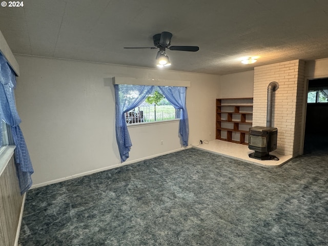 unfurnished living room with ceiling fan, dark colored carpet, plenty of natural light, and a wood stove