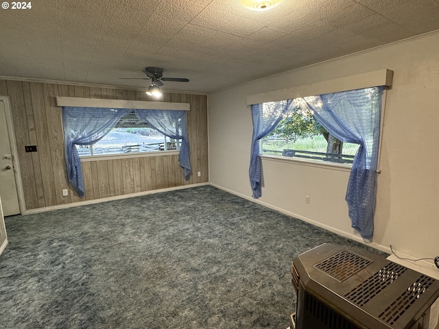 interior space featuring baseboards, ceiling fan, a textured ceiling, wood walls, and dark carpet