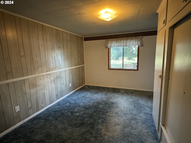 unfurnished room featuring crown molding, dark colored carpet, and wooden walls