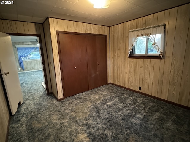 unfurnished bedroom featuring multiple windows, dark colored carpet, a closet, and wooden walls