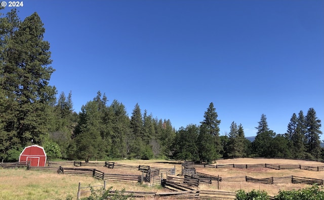 view of yard featuring fence, an outdoor structure, and a rural view