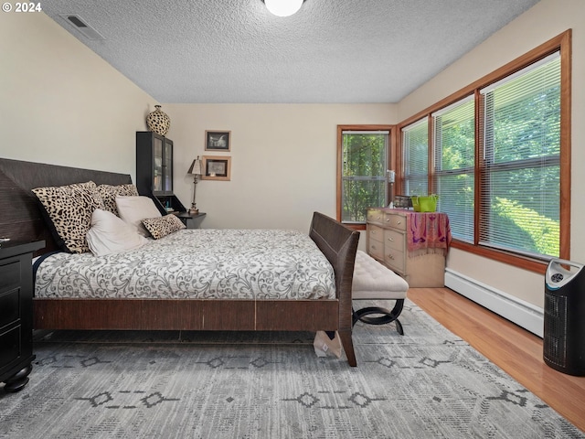 bedroom featuring hardwood / wood-style floors, baseboard heating, and a textured ceiling