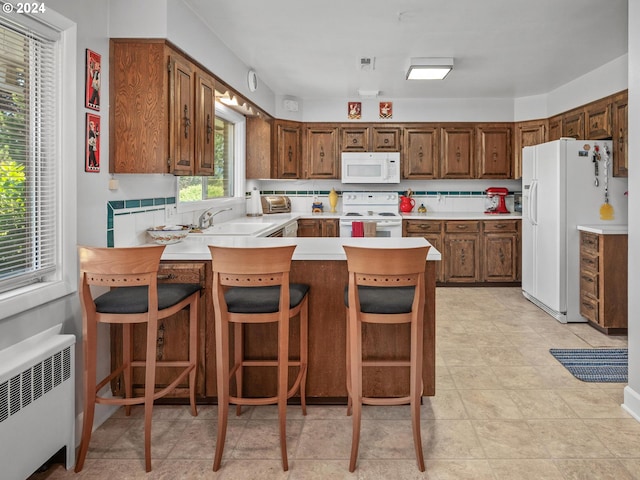 kitchen with radiator, kitchen peninsula, white appliances, a breakfast bar area, and decorative backsplash