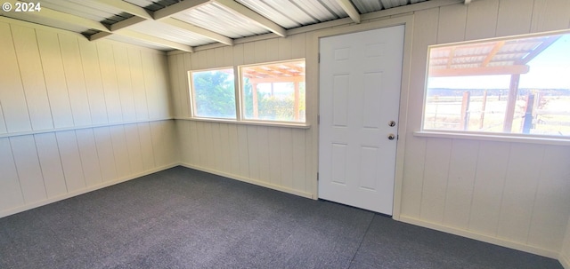 unfurnished room featuring beamed ceiling, wooden walls, and a healthy amount of sunlight