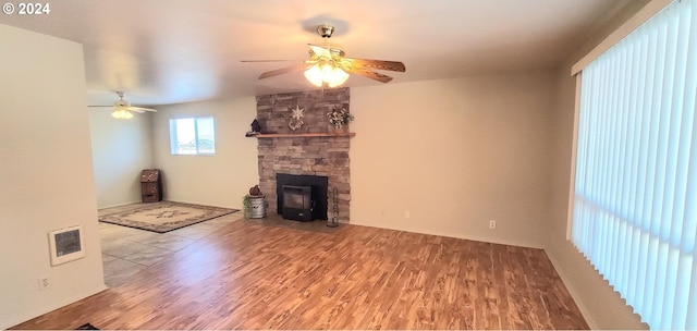 unfurnished living room featuring a wood stove, hardwood / wood-style flooring, and ceiling fan