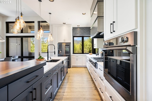 kitchen featuring sink, white cabinetry, wall chimney exhaust hood, hanging light fixtures, and appliances with stainless steel finishes