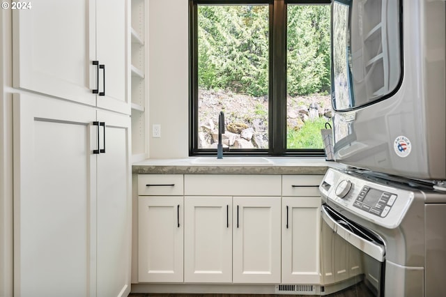 kitchen featuring white cabinets, stacked washing maching and dryer, a wealth of natural light, and sink