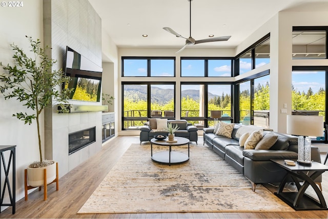 living room featuring a tiled fireplace, ceiling fan, light hardwood / wood-style flooring, and a towering ceiling