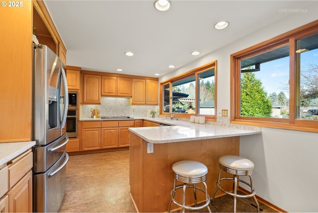 kitchen with backsplash, a kitchen breakfast bar, light stone counters, kitchen peninsula, and stainless steel appliances