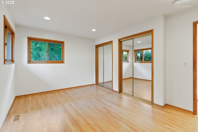 unfurnished bedroom featuring multiple closets and light wood-type flooring