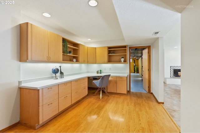 kitchen with built in desk, light brown cabinets, a textured ceiling, and light wood-type flooring