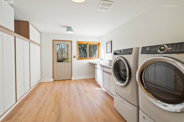 laundry room featuring cabinets, washing machine and dryer, and light wood-type flooring