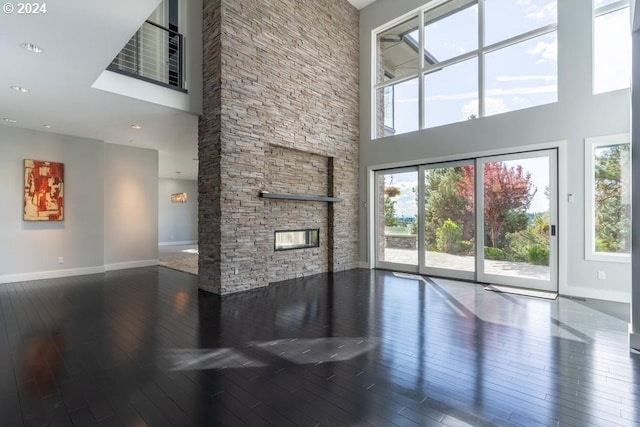 unfurnished living room with baseboards, a stone fireplace, hardwood / wood-style floors, and a towering ceiling