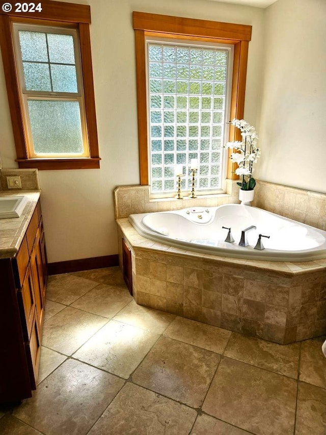 bathroom featuring a wealth of natural light, vanity, and tiled tub