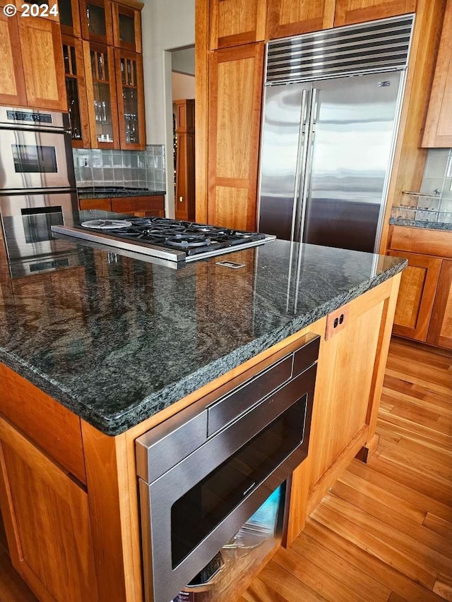 kitchen featuring light hardwood / wood-style flooring, dark stone countertops, appliances with stainless steel finishes, and decorative backsplash