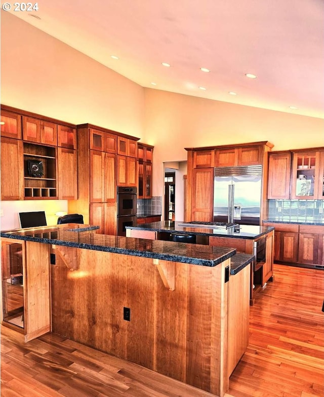 kitchen featuring dark stone countertops, light hardwood / wood-style floors, stainless steel appliances, a kitchen breakfast bar, and a large island