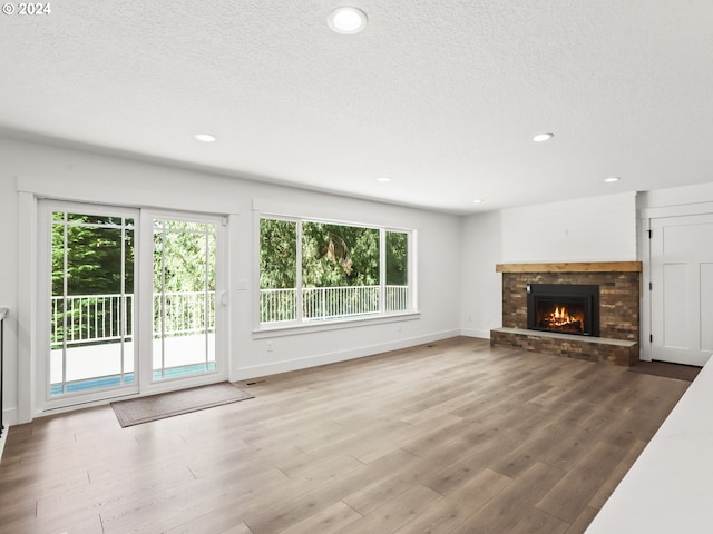 unfurnished living room featuring hardwood / wood-style flooring, a stone fireplace, and a textured ceiling