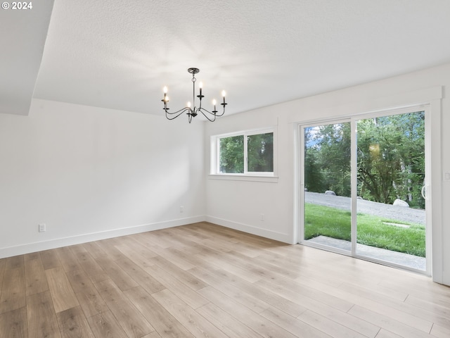 unfurnished dining area featuring a chandelier, light hardwood / wood-style flooring, and a textured ceiling