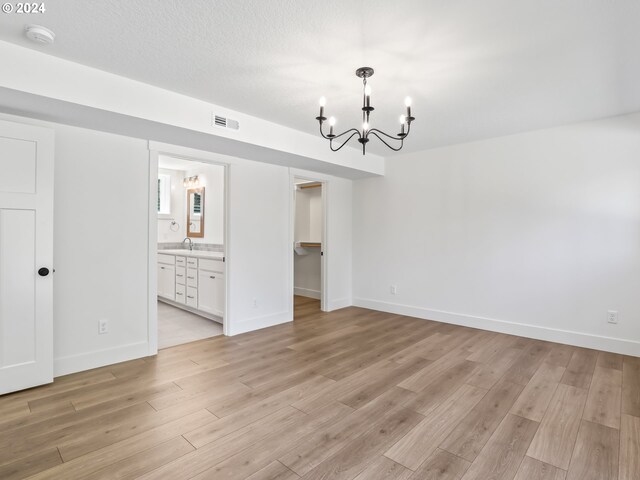 unfurnished dining area featuring a notable chandelier, sink, a textured ceiling, and light wood-type flooring