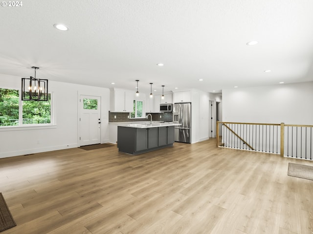 kitchen with white cabinetry, hanging light fixtures, stainless steel appliances, and a center island with sink