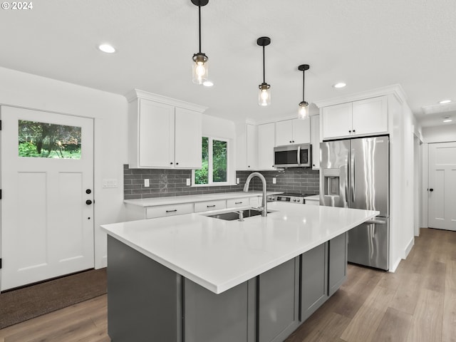 kitchen featuring white cabinetry, hanging light fixtures, a kitchen island with sink, and appliances with stainless steel finishes