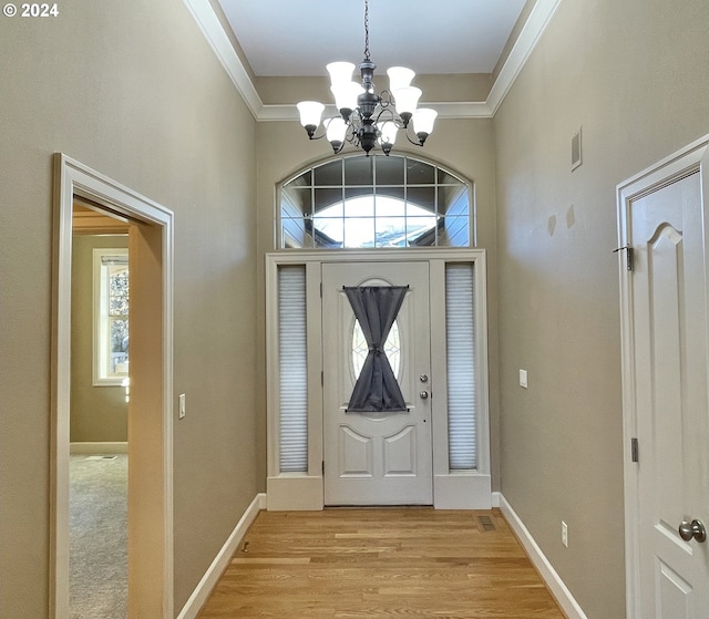 foyer entrance featuring light hardwood / wood-style flooring, crown molding, a wealth of natural light, and a chandelier