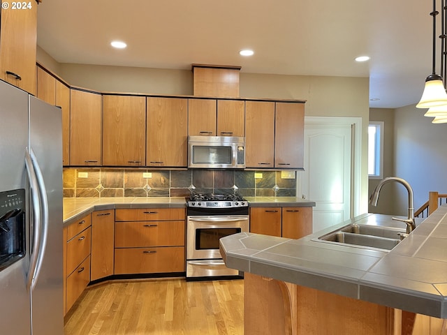 kitchen with stainless steel appliances, sink, tile countertops, and decorative light fixtures