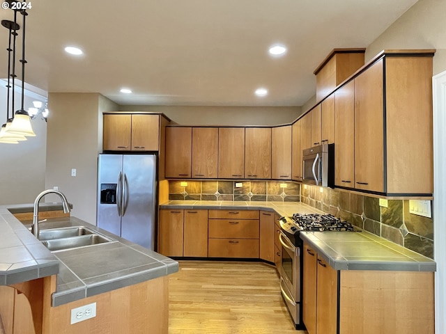 kitchen with pendant lighting, sink, stainless steel appliances, tile counters, and light wood-type flooring