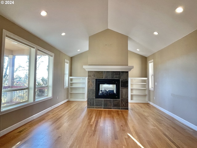 unfurnished living room featuring a tile fireplace, lofted ceiling, and light wood-type flooring