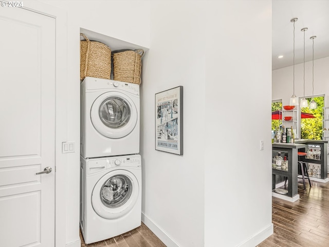 clothes washing area featuring baseboards, wood finished floors, laundry area, and stacked washing maching and dryer