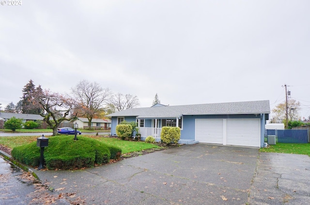 ranch-style home featuring a front yard, a garage, covered porch, and cooling unit