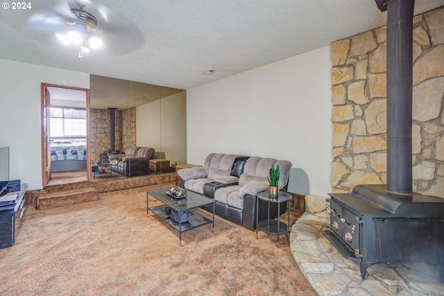 living room with a textured ceiling, carpet, ceiling fan, and a wood stove