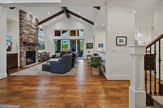 living room featuring hardwood / wood-style floors, beam ceiling, a stone fireplace, and high vaulted ceiling